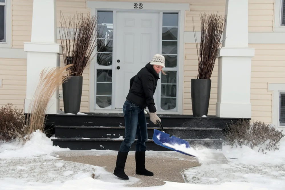 Snøskuffe lent mot en hvit inngangsdør etter nattens snøfall